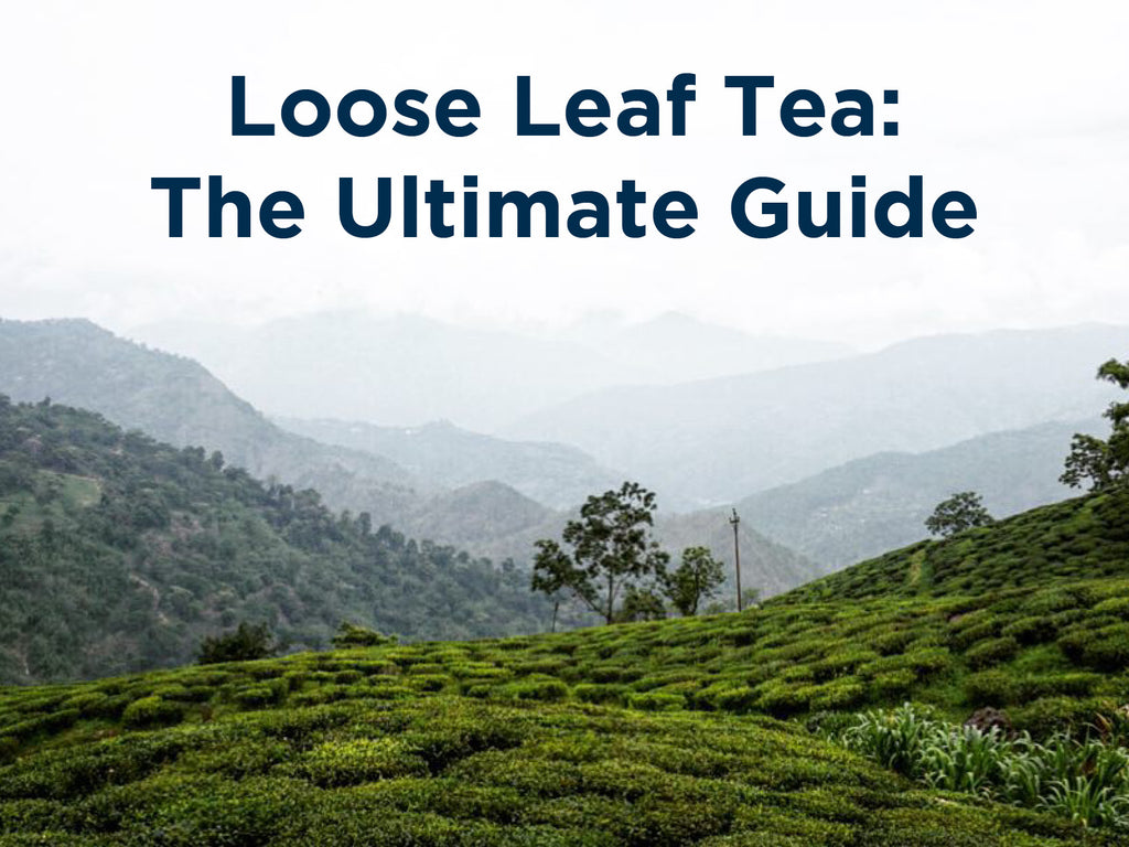 An full hd picture with a full cup of green tea with a tea bag in it and a  tea leaves around it and a beautiful landscape of mountains in the  background