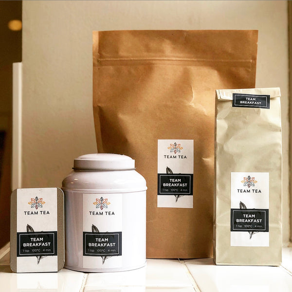 Team Tea's 4 packaging sizes lined up against a white wall. On the left is the slide tin, then the white caddy (Regular tin), in the back is the 250g refill and front right is the 100g refill.