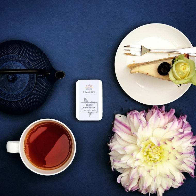 A tin containing loose-leaf decaffeinated black tea with a white label and a botanical sketch of a tea plant.