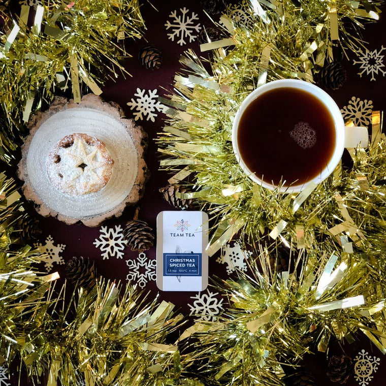 A silver metal tin against a white background. The tin is labelled Christmas Spiced tea and contains loose-leaf tea leaves.