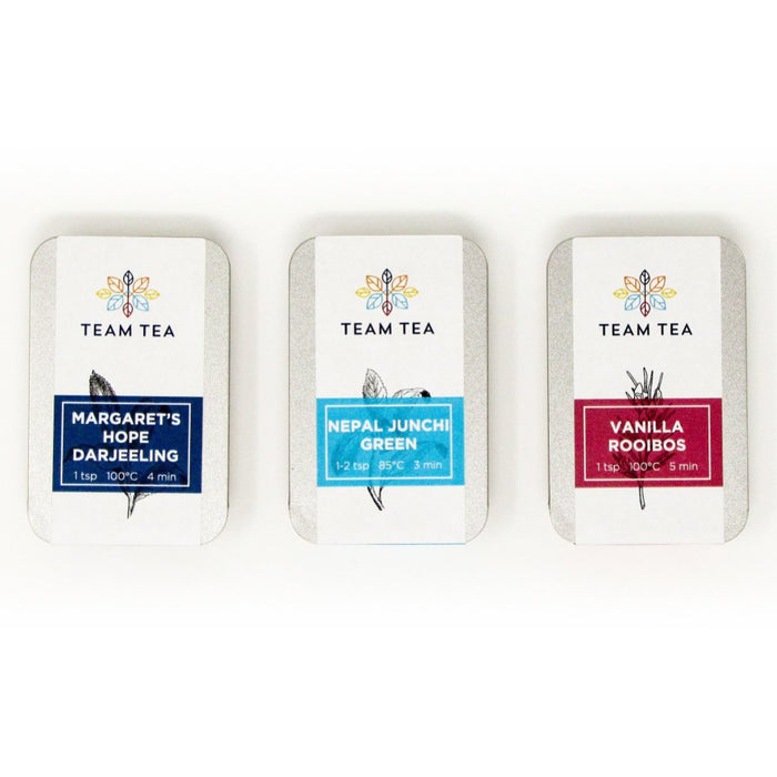 3 metal tins sit side by side on a white background. The left tin has a navy blue label, the middle a turquoise label, and the right a red one.