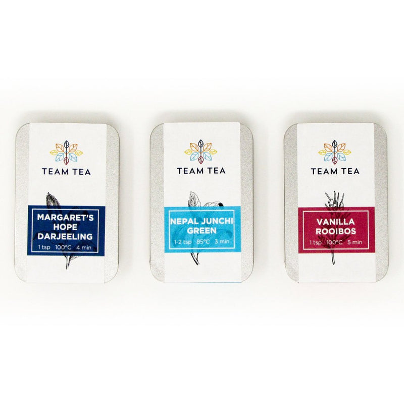 3 metal tins sit side by side on a white background. The left tin has a navy blue label, the middle a turquoise label, and the right a red one.
