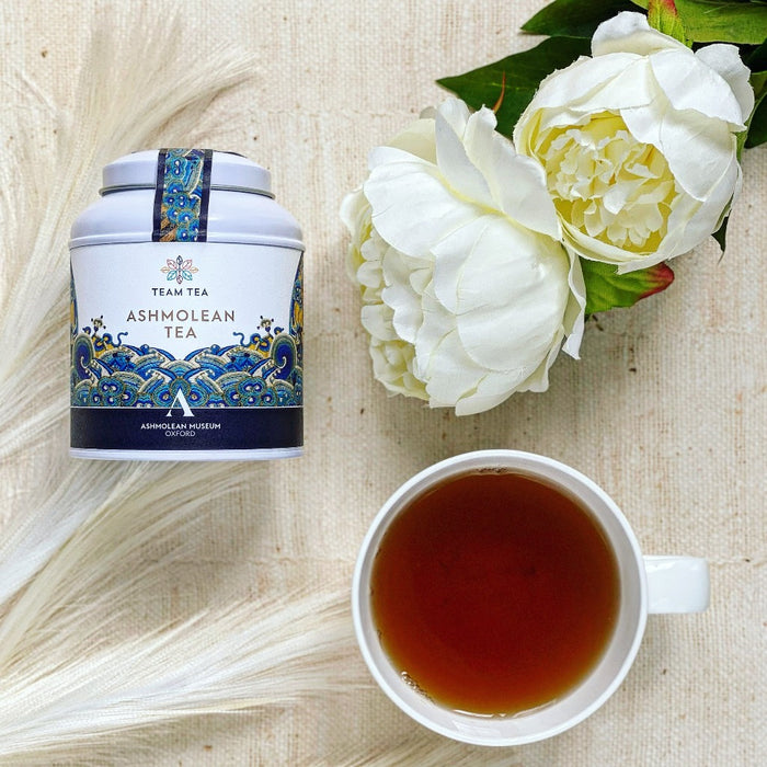 Image of Ashmolean Tea Caddy with a cup of brewed tea and white flowers on a textured background