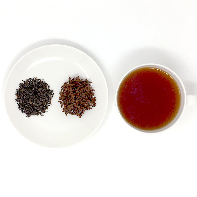 A cup of brewed black tea sits next to a plate of loose leaf teas, showing the dry leaf and then the brewed wet leaf.