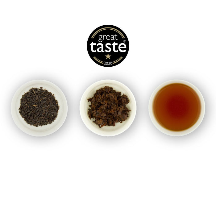 Three circular bowls arranged in a row with the middle bowl containing a brewed tea sample, flanked by two bowls with dry tea leaves on the left and brewed tea liquid on the right, and a 'Great Taste' award seal at the top centre.