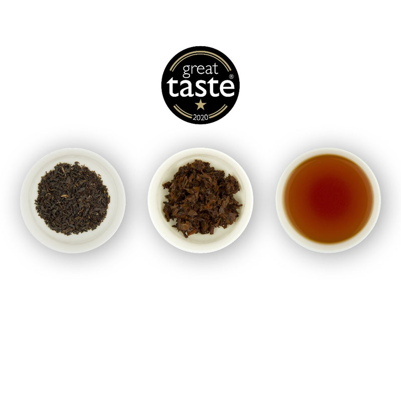 Three circular bowls arranged in a row with the middle bowl containing a brewed tea sample, flanked by two bowls with dry tea leaves on the left and brewed tea liquid on the right, and a 'Great Taste' award seal at the top centre.