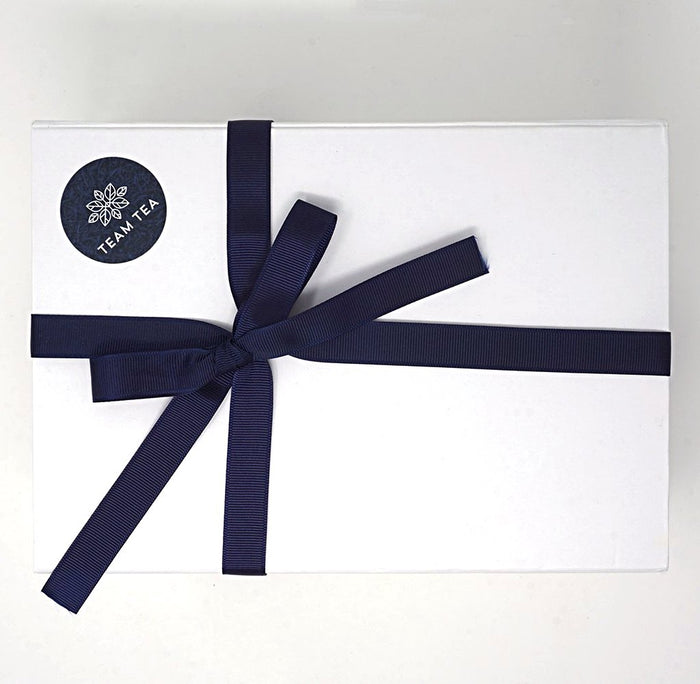 A white gift box with a navy blue ribbon and a brand logo on the top left corner.