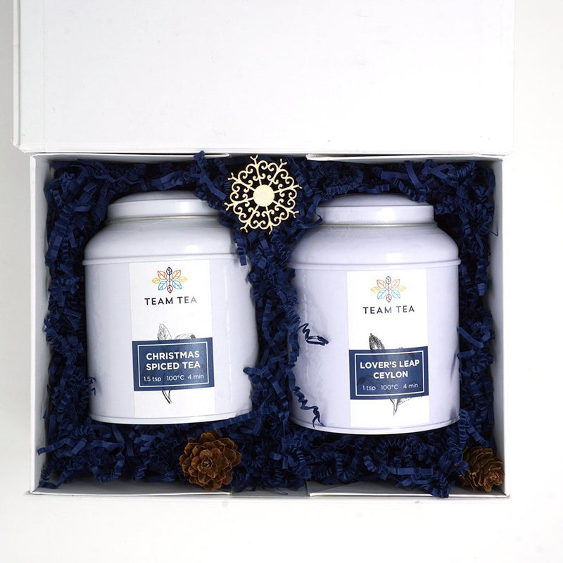 A rectangular white gift box, filled with navy blue shredded paper and 2 caddies of loose-leaf black tea