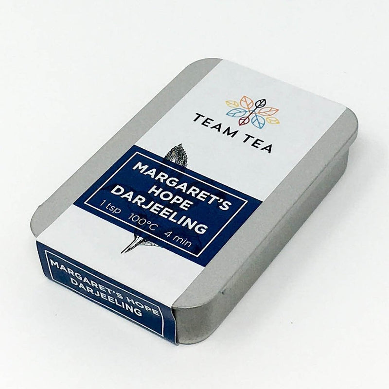A metal tin containing loose-leaf Darjeeling tea. The tin has a paper label with a blue banner and text Margaret's Hope Darjeeling