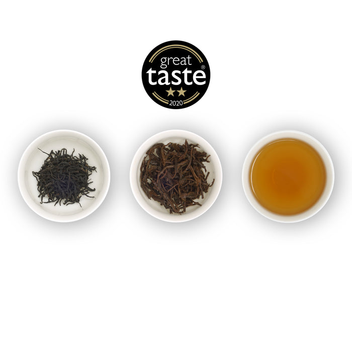 Three white bowls arranged side by side with the left bowl containing dry tea leaves, the middle bowl showing wet tea leaves, and the right bowl displaying brewed tea. Above is the Great Taste Award winners logo