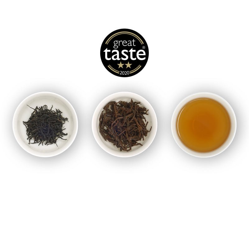 Three white bowls arranged side by side with the left bowl containing dry tea leaves, the middle bowl showing wet tea leaves, and the right bowl displaying brewed tea. Above is the Great Taste Award winners logo