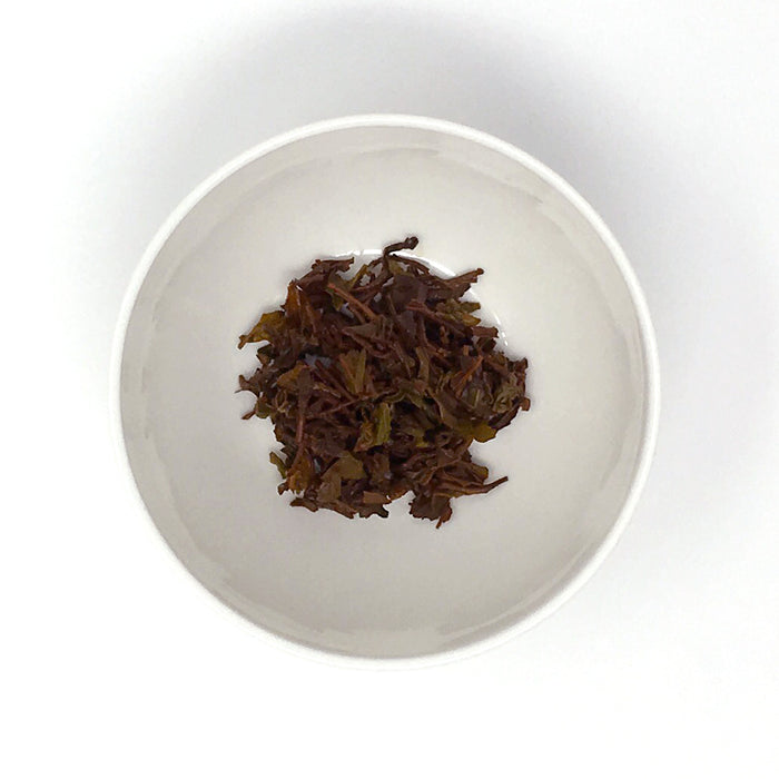 A close up of a small white porcelain ramekin with brewed (wet) black tea leaves (loose-leaf)