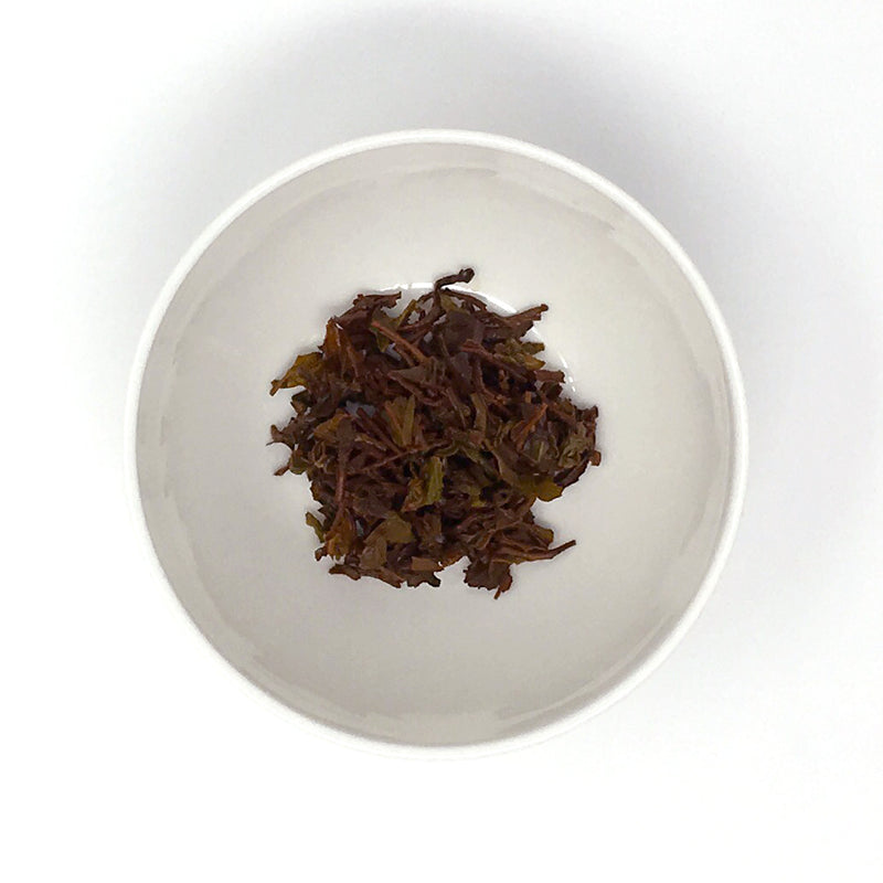 A close up of a small white porcelain ramekin with brewed (wet) black tea leaves (loose-leaf)