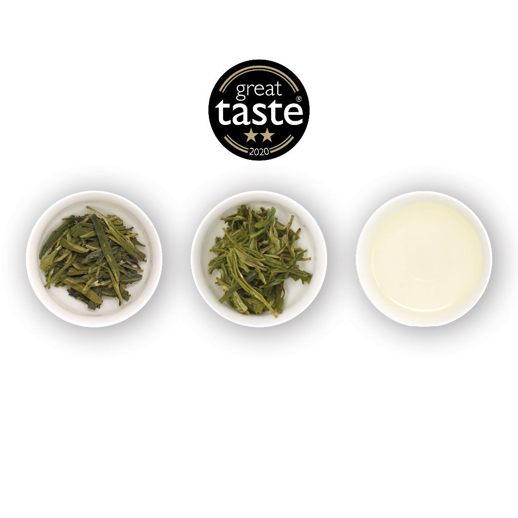 Three white bowls containing loose-leaf green tea leaves and a cup with brewed tea liquid, with a 'Great Taste Awards' winners badge displayed above.