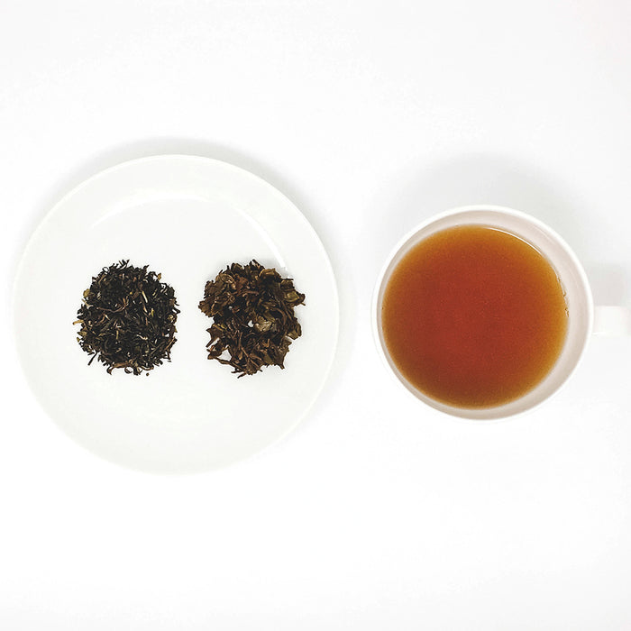 A cup of brewed Darjeeling black tea sits next to a plate of loose leaf teas, showing the dry leaf and then the brewed wet leaf.