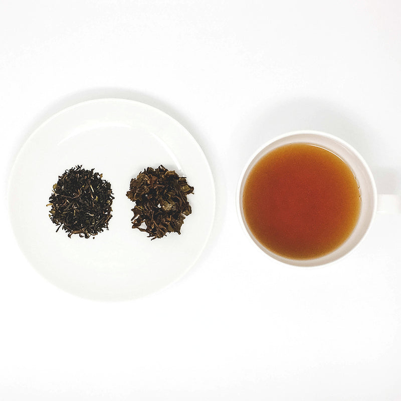 A cup of brewed Darjeeling black tea sits next to a plate of loose leaf teas, showing the dry leaf and then the brewed wet leaf.