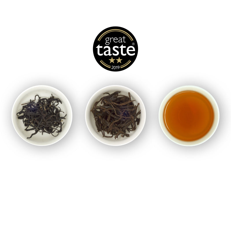 Three circular bowls arranged side by side with the left bowl containing dry tea leaves, the middle bowl showing wet tea leaves, and the right bowl displaying a cup of brewed black tea. Above is the Great Taste Awards logo