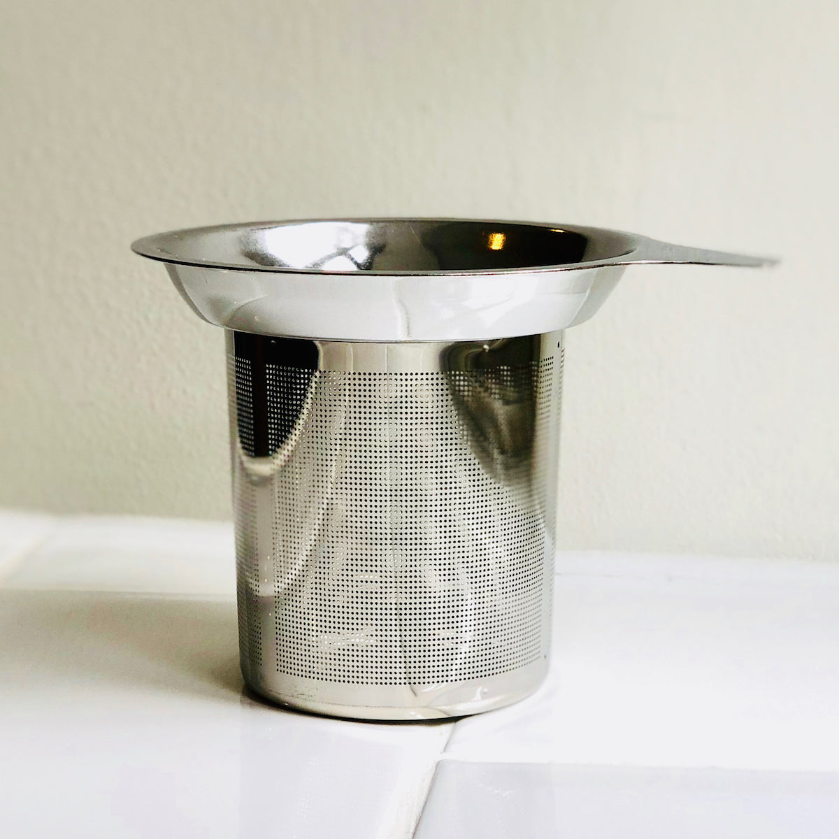 A stainless steel tea strainer basket designed to fit in a mug or teapot.