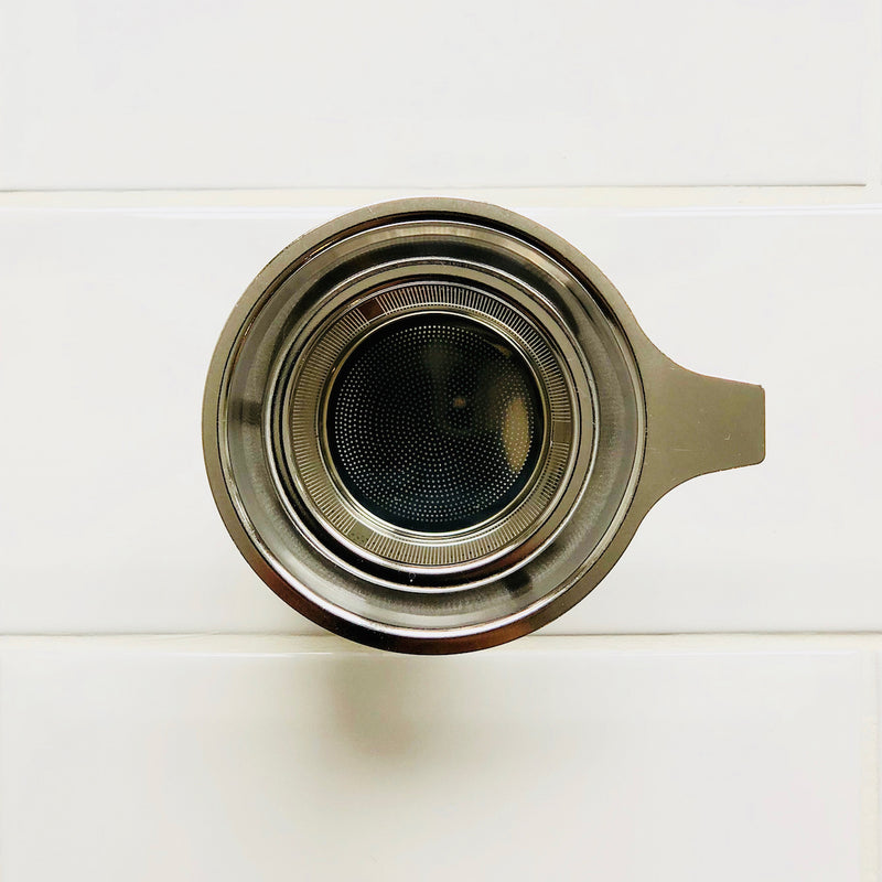 An overhead shot of a stainless steel tea infuser (Strainer) basket with a pattern of fine holes.