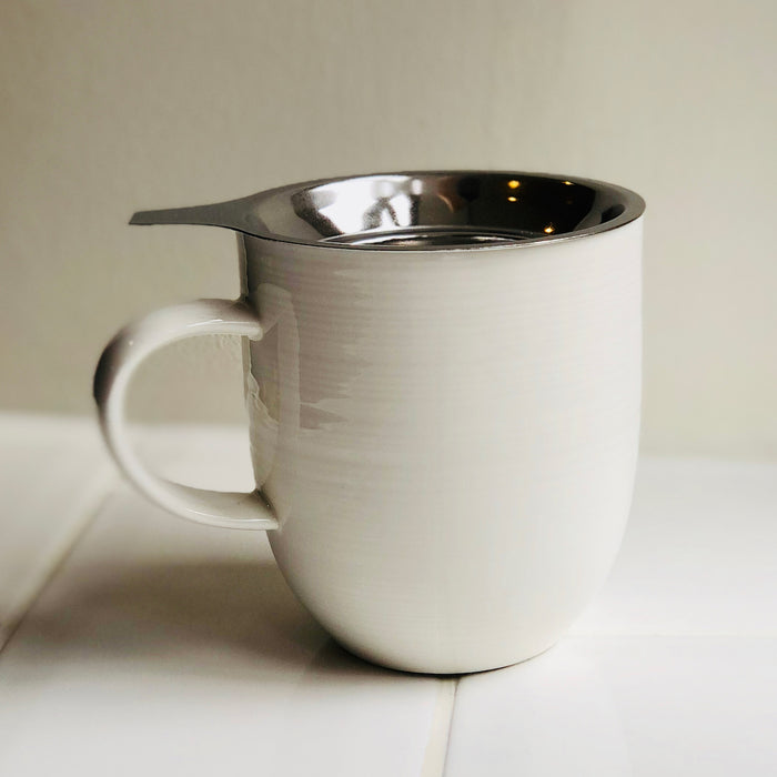 A stainless steel tea strainer sits neatly inside a porcelain mug ready to brew loose-leaf tea.