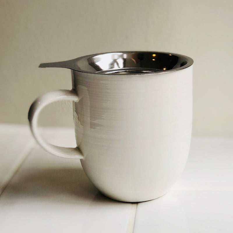 A stainless steel tea strainer sits neatly inside a porcelain mug ready to brew loose-leaf tea.