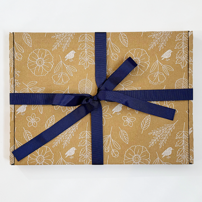 Gift box with floral and bird pattern wrapped in brown paper with a blue ribbon on a white background