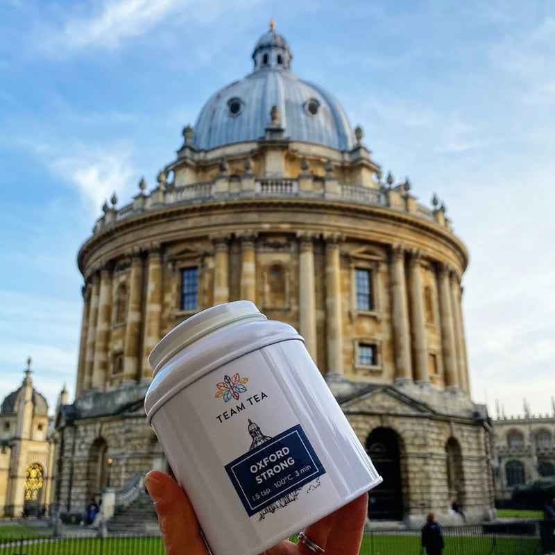 Caddy of Oxford Strong tea held up with Radcliffe Camera (Oxford) in the background and a bright blue sky