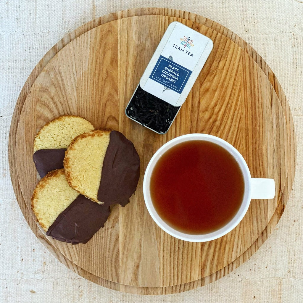 Board with 3 shortbreads dipped in chocolate, a cup of tea and a tin of Black Emerald Colombia